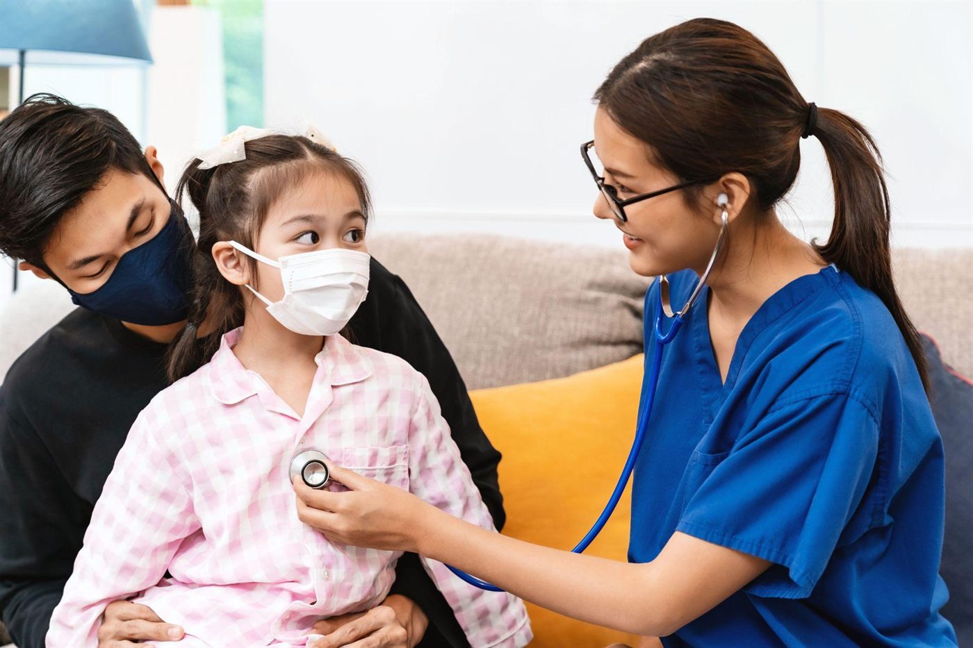 A paediatrician listening to a young child's chest while a parent holds her