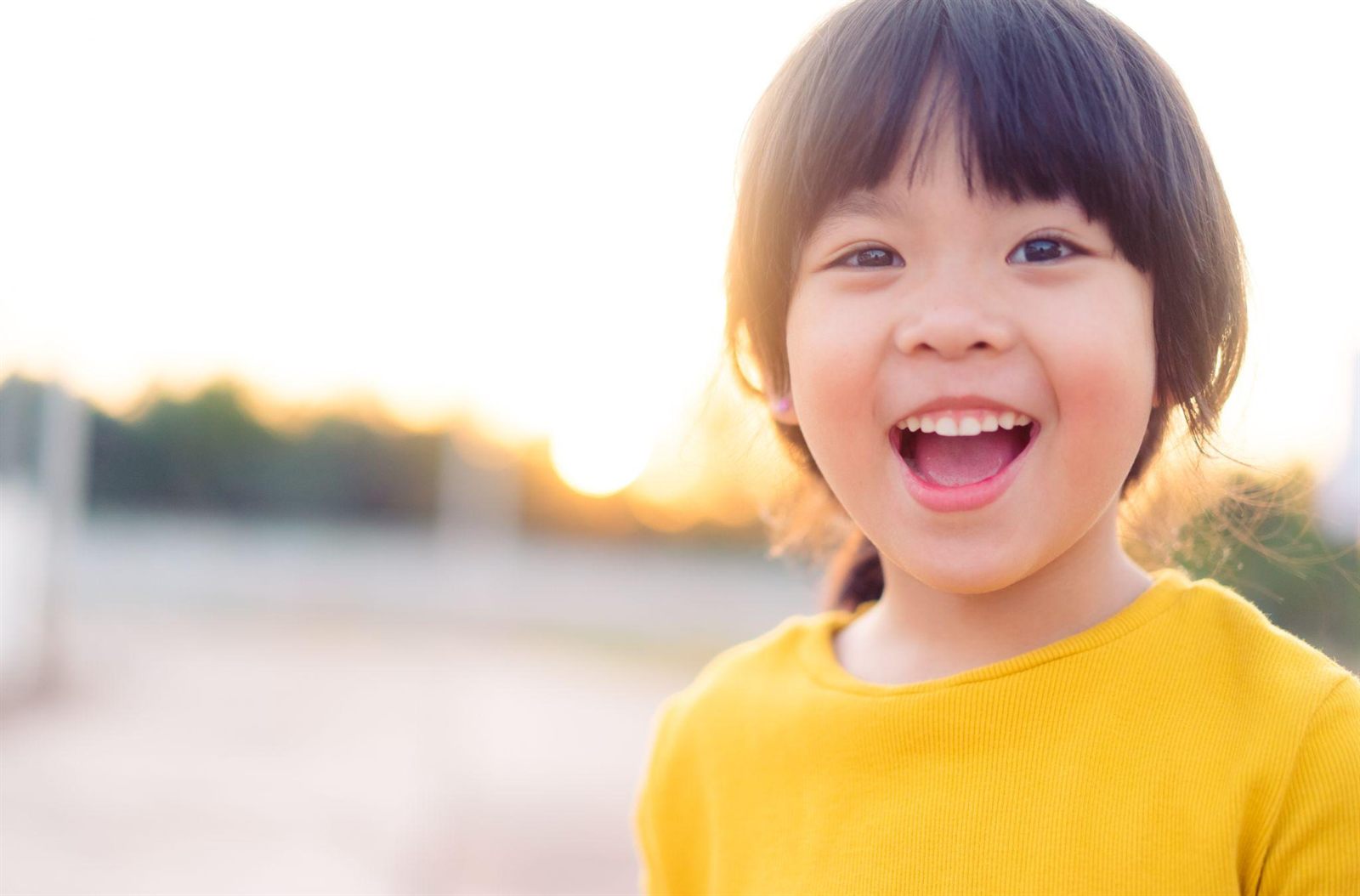 A smiling young child outdoors at sunset