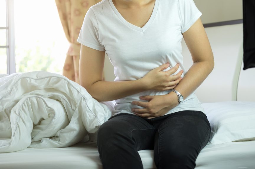 A woman sitting on the edge of a bed, holding her abdomen